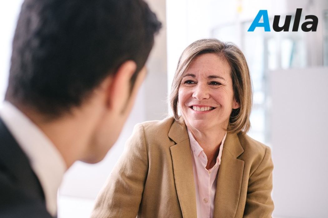 Dues persones conversant en un entorn professional amb el logotip d&rsquo;Aula visible a la cantonada superior dreta