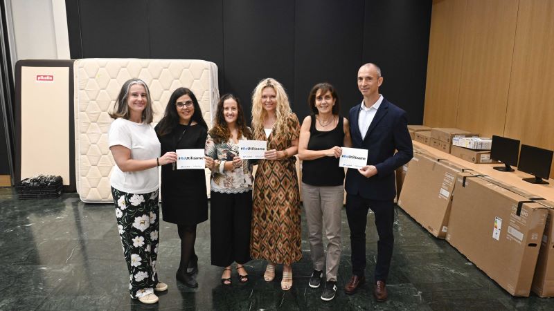 Cinc persones sostenen cartells de ReUtilitza&rsquo;m amb alguns materials donats al fons