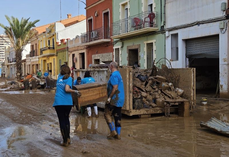 Tres voluntaris realitzen tasques de neteja despr&eacute;s de la DANA de Val&egrave;ncia en un carrer ple de fang.