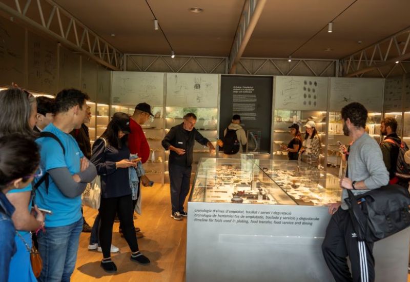 Un grup escolta un guia que explica utensilis de cuina exposats en una vitrina.