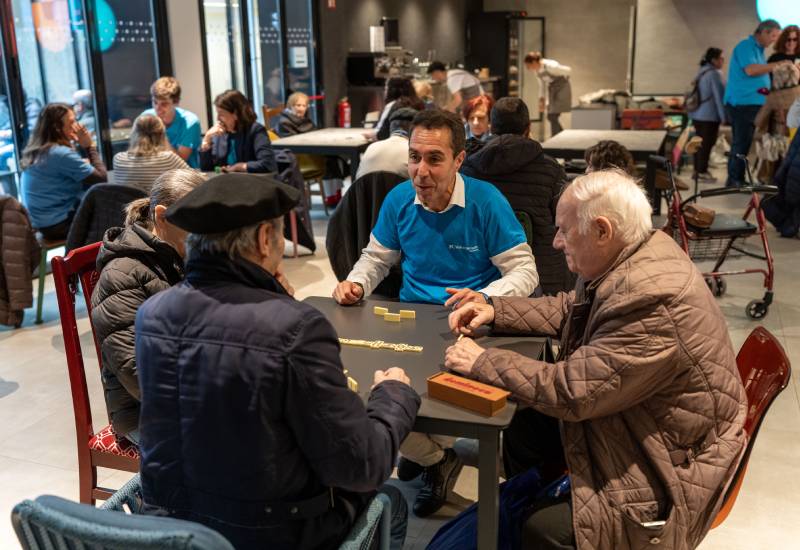 Tres homes grans juguen al domin&oacute; amb un voluntari de CaixaBank en una resid&egrave;ncia a Bilbao
