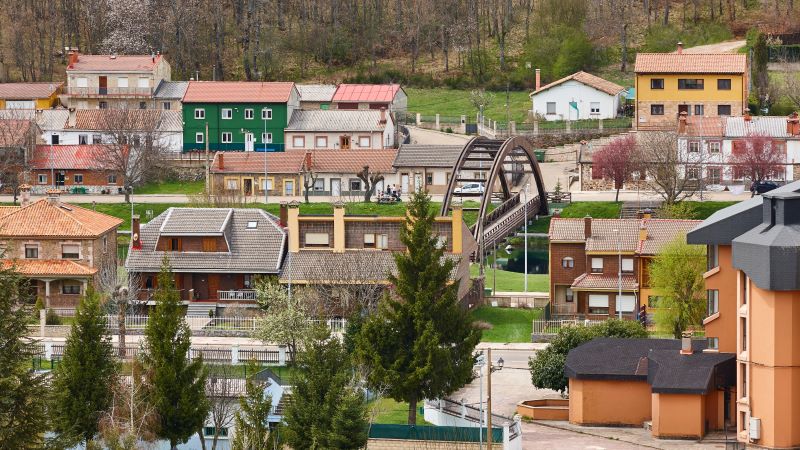 Velilla del Río Carrión: naturalesa i senderisme a la Montaña Palentina Vista de Velilla del Río Carrión amb cases de colors i teulades vermelles, carrers arbrats i un pont metàl·lic sobre el riu en entorn muntanyós