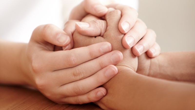 CaixaBank ofereix acompanyament integral a persones amb necessitats especials Mans entrellaçades de diverses persones sobre una taula de fusta, en un gest de suport i acompanyament proper