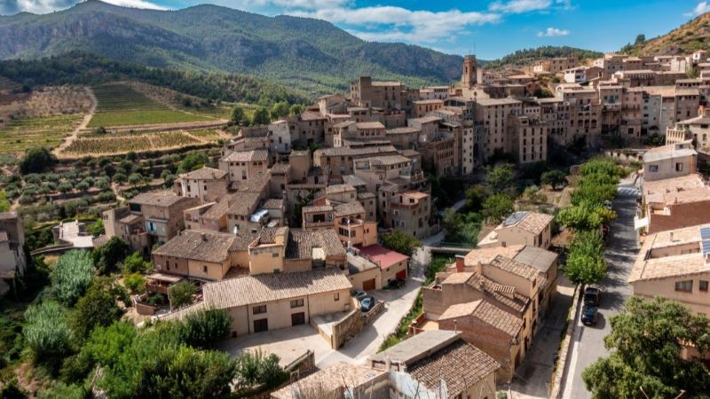 La Vilella Baixa (Tarragona): la ‘Nova York del Priorat’ Vista de la Vilella Baixa amb cases de pedra agrupades en un vessant, envoltades de muntanyes, vinyes i vegetació, sota cel blau amb núvols