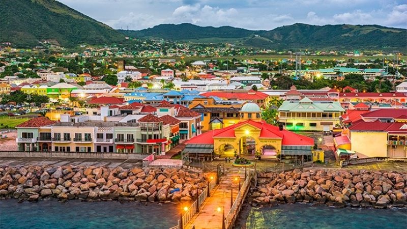 Saint Kitts i Nevis és el país més petit d’Amèrica per superfície. Vista de Saint Kitts i Nevis, ciutat costanera amb edificis de colors vora el mar i muntanyes al fons