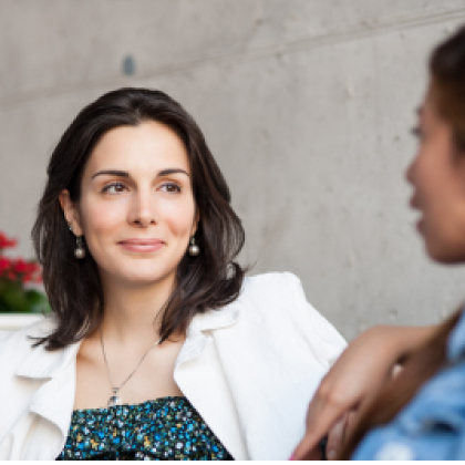 La imagen muestra a dos mujeres conversando. La mujer en primer plano está enfocada y mirando hacia la otra mujer que sale de lado desenfocada.