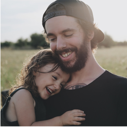 Hombre con su hija en brazos sonrientes con un campo de fondo