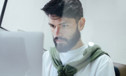 Chico joven con barba concentrado consultando el ordenador