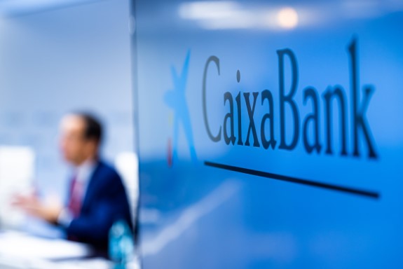 Pantalla de televisión con el logotipo de CaixaBank y una conferencia de fondo