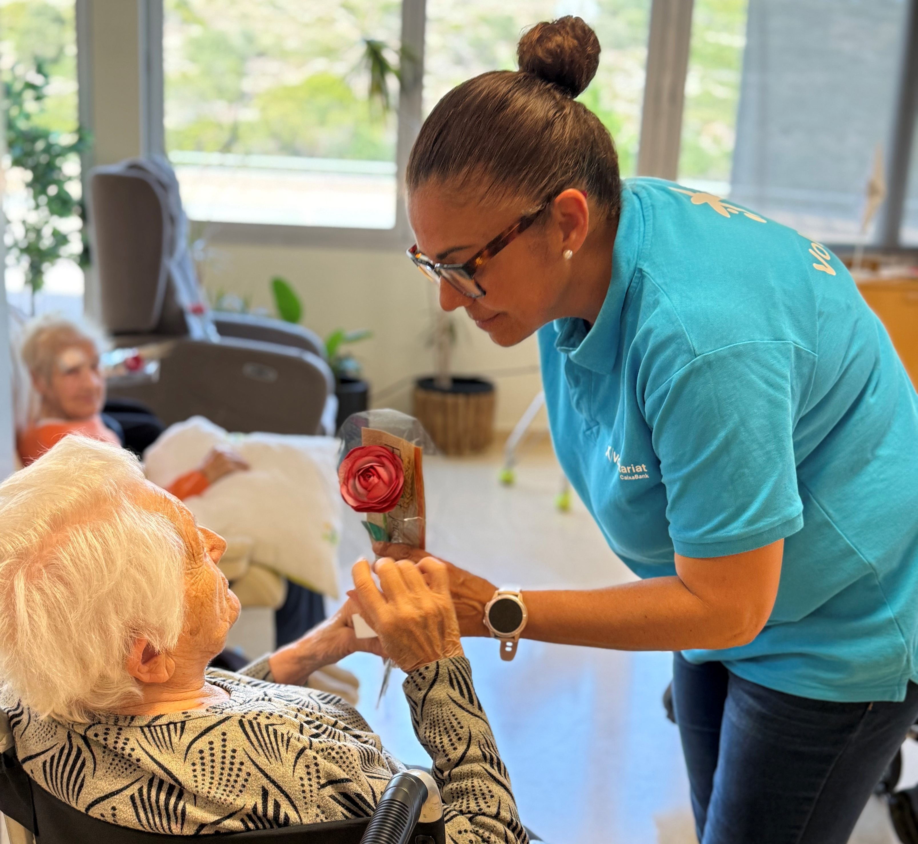  Imagen de una voluntaria de CaixaBank durante la entrega de rosas a una mujer mayor en la Residencia Llevant de Tarragona.