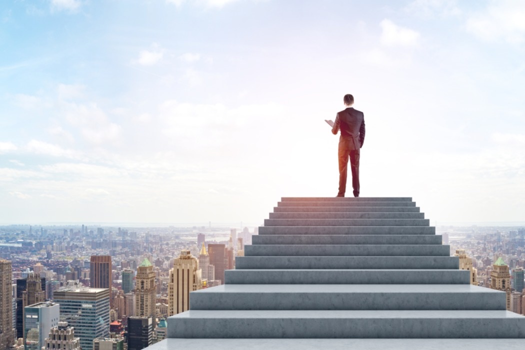 Empresario en la cima de una escalera con una gran ciudad a sus pies