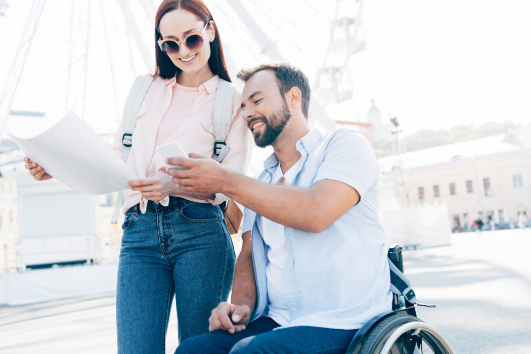 Un turista en silla de ruedas le enseña un smartphone a su compañera mientras recorren la ciudad