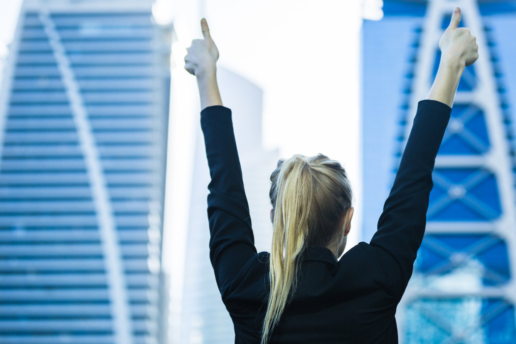 Jove fent senyal de triomf davant d'edificis d'empreses