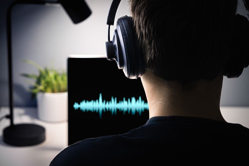 Un hombre con auriculares mira unas ondas sonoras en un monitor de ordenador