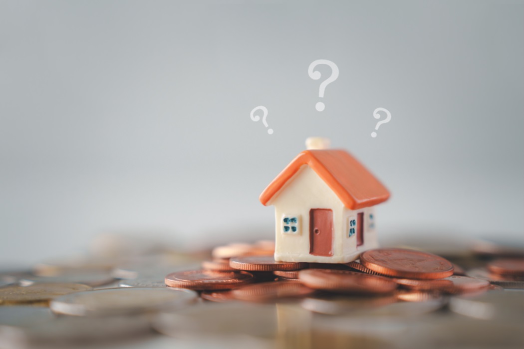 Una casa de joguina sobre monedes amb signes d'interrogació al voltant