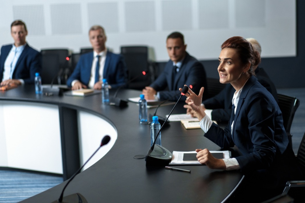 Una mujer directiva habla sentada en una mesa de consejo ante la mirada de tres ejecutivos