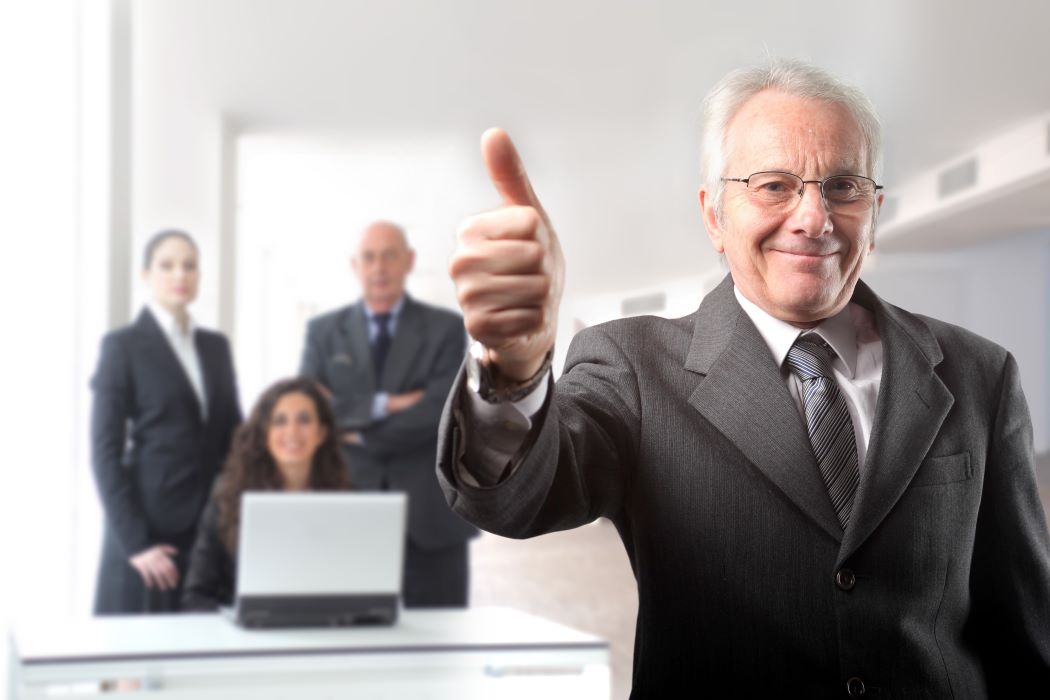 Hombre de negocios sénior con el pulgar hacia arriba delante de un grupo de empresarios