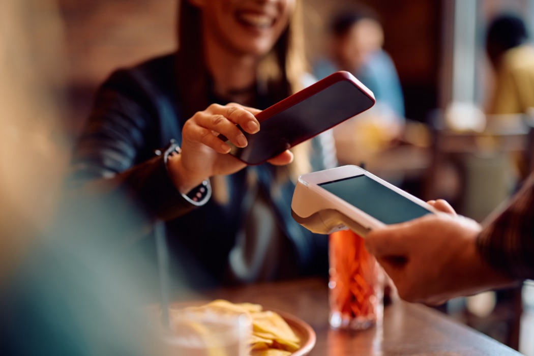 Una dona paga amb contactless a través del telèfon mòbil en un bar. 