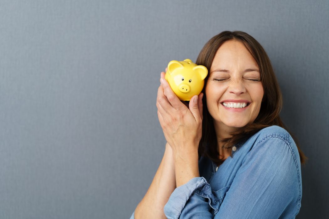 Joven feliz abrazada a una hucha amarilla con forma de cerdo