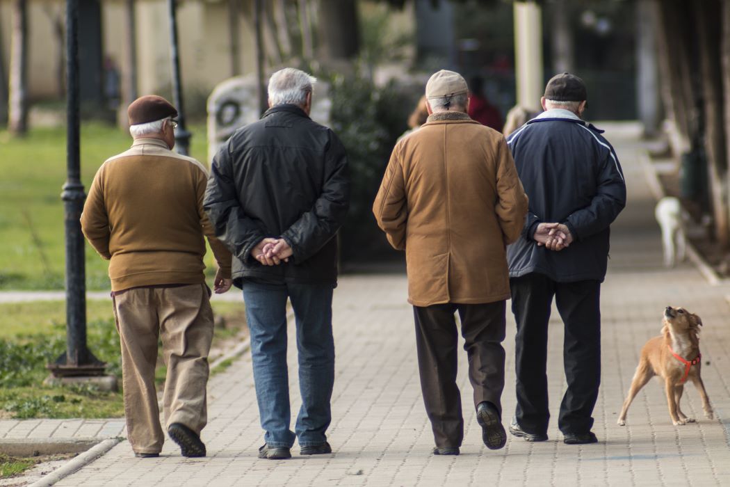 Cuatro hombres mayores caminan de espaldas por un boulevard