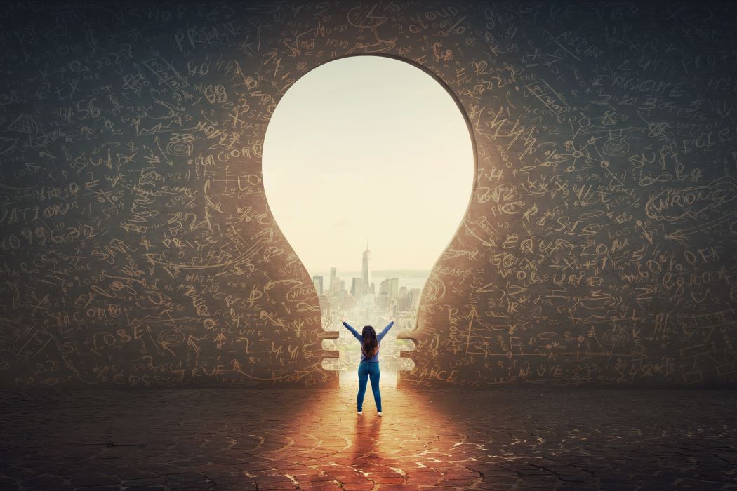 Una dona aixeca les mans davant la silueta d’una bombeta dibuixada en un mur de formigó.