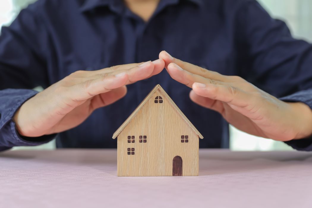 Concepto de vivienda protegida: unas manos protegen una casa de juguete