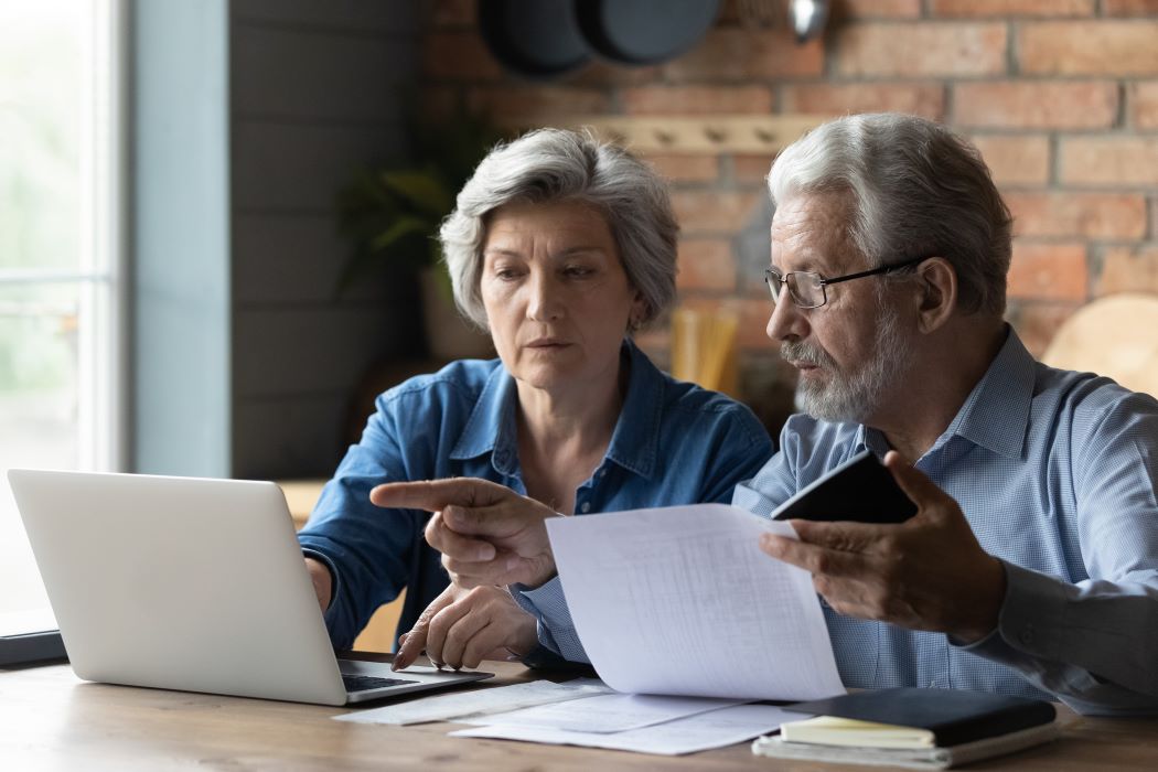Parella gran revisa documents i gestiona tràmits en un portàtil mentre consulta papers junts