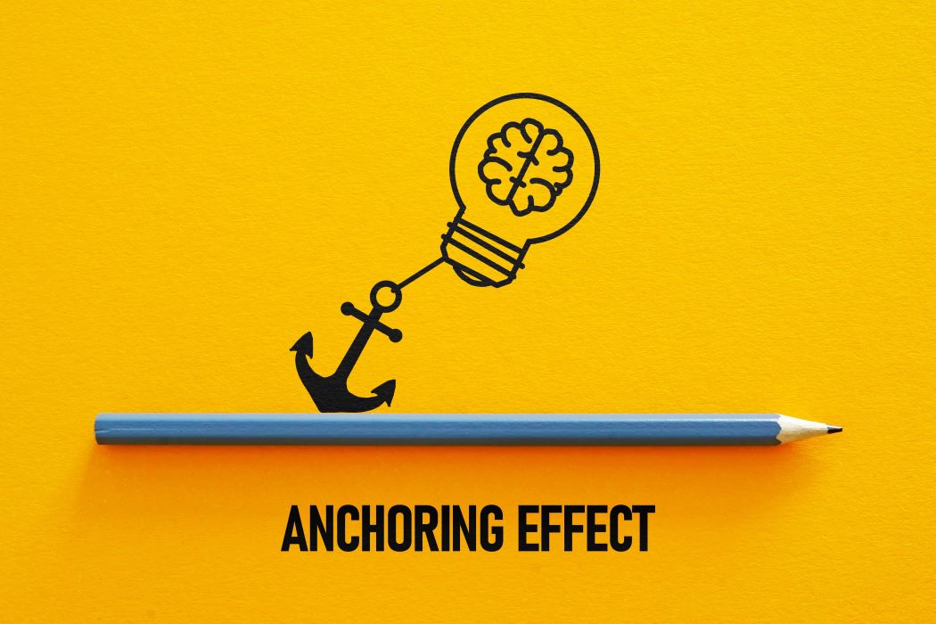 Ilustración de una bombilla con cerebro unida a un ancla sobre fondo amarillo con el texto ‘Anchoring Effect’.