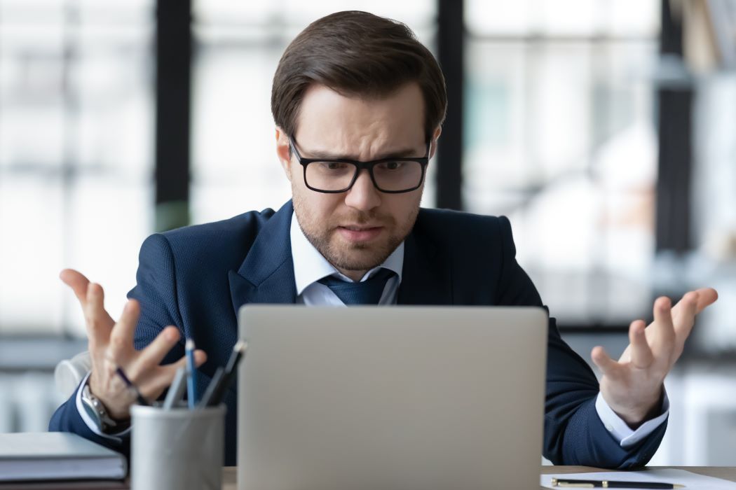 Persona con traje gesticulando delante del portátil en una oficina luminosa