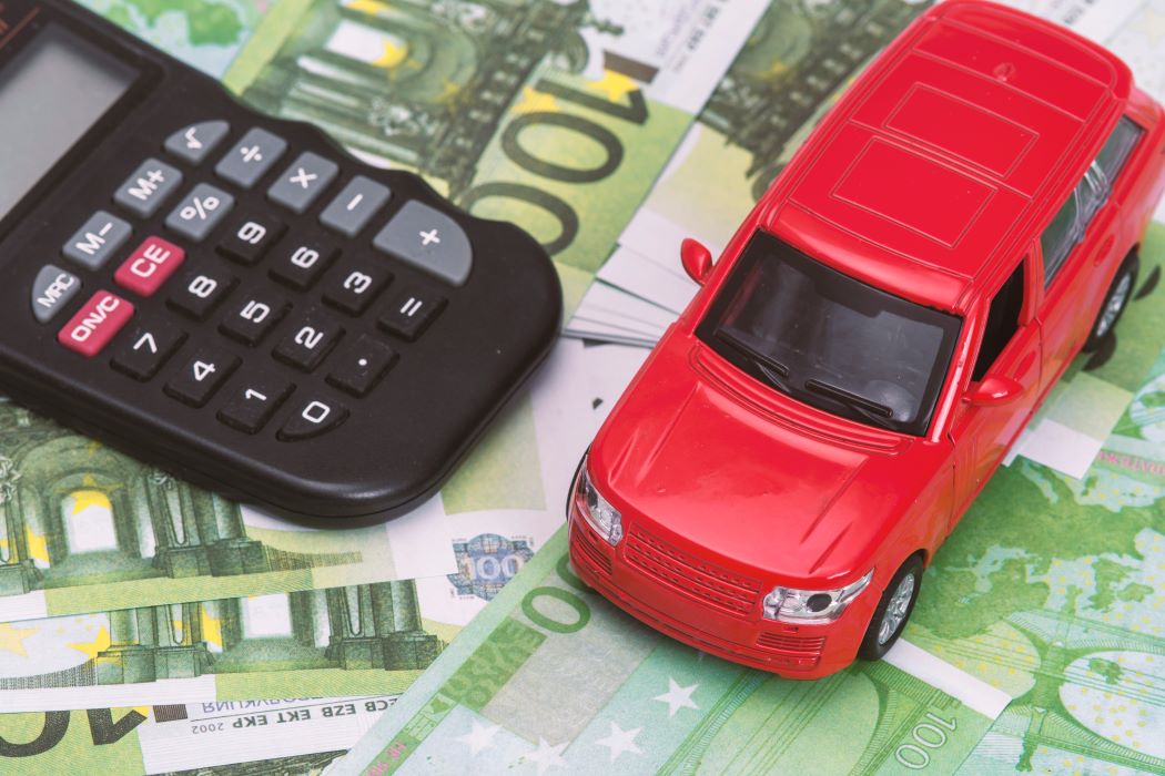 Coche rojo de juguete y calculadora sobre billetes de euro.