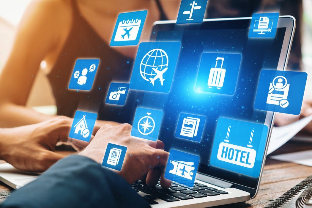 Manos utilizando un portátil mientras varios iconos digitales de servicios de viaje, vuelos y hoteles aparecen flotando sobre la pantalla