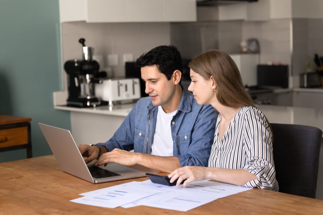Parella revisant documents i dades financeres en una taula mentre consulten informació en un ordinador portàtil a casa seva