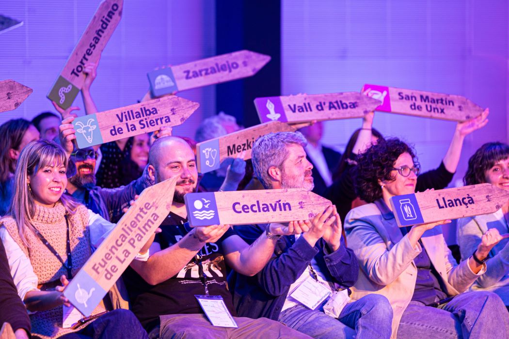 Grupo de personas sosteniendo carteles de madera con nombres de distintos municipios durante un evento de Tierra de oportunidades