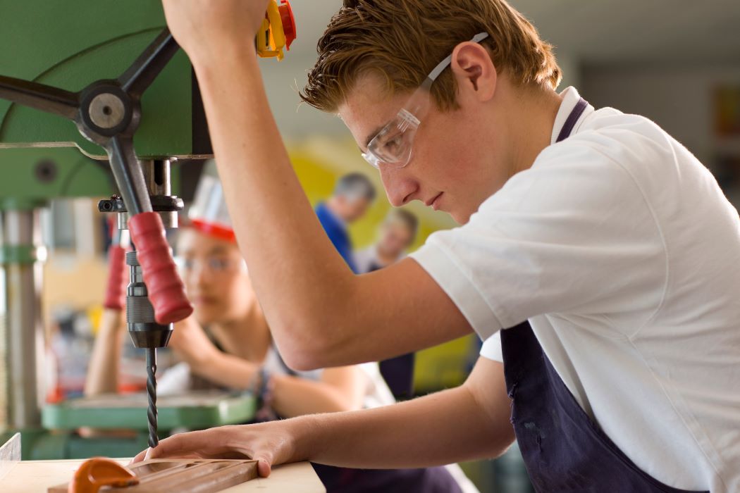 Joven trabajando en un taller utiliza una taladradora de columna para perforar una pieza de madera