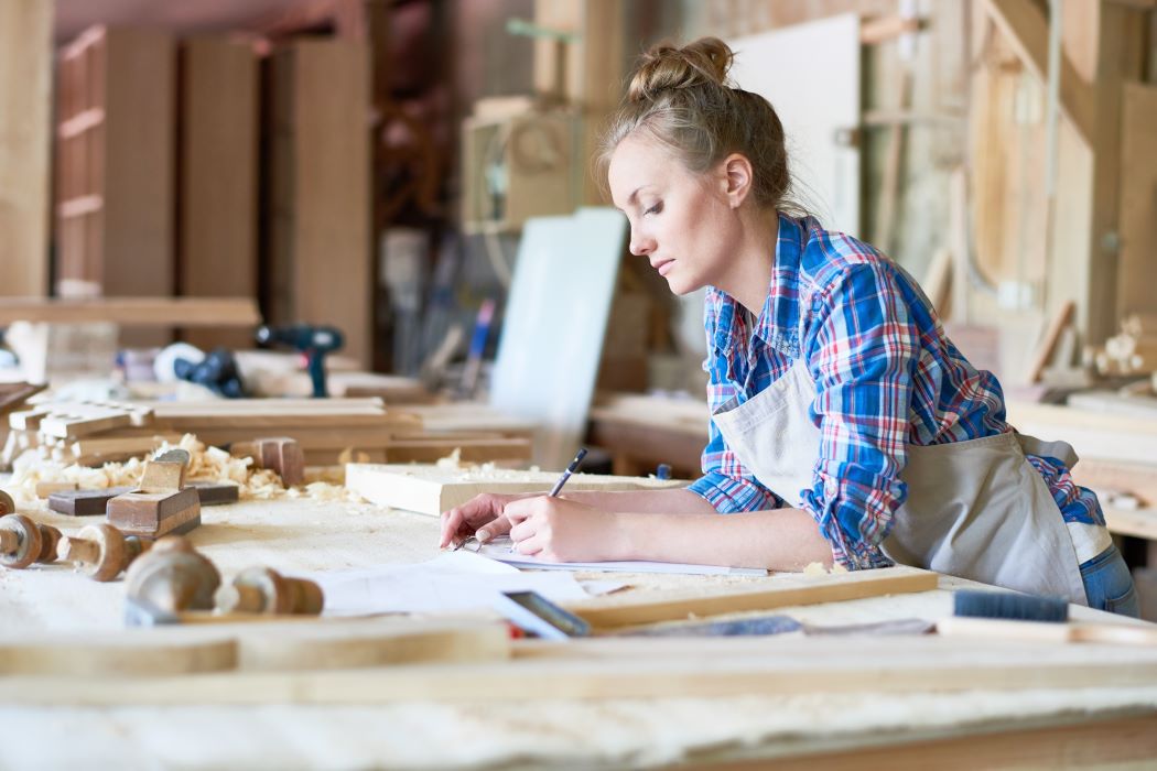 Emprendedora trabajando la madera en un taller, haciendo mediciones y dibujos sobre una mesa de carpintería