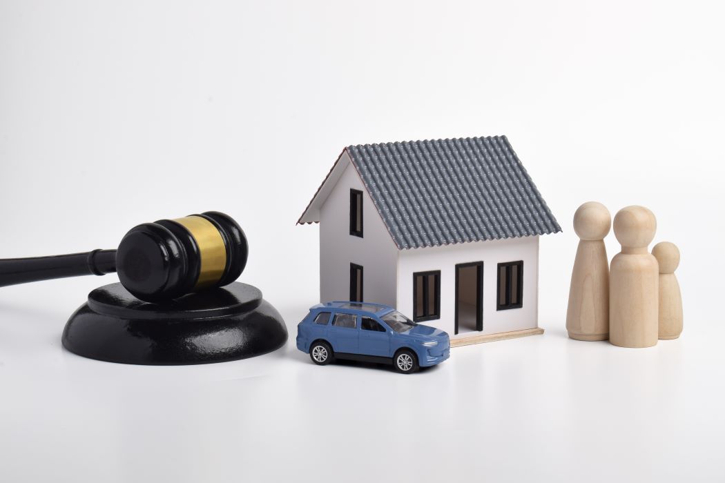 Composición con un mazo judicial, una vivienda, un coche y varias figuras de madera que representan un núcleo familiar, sobre fondo blanco