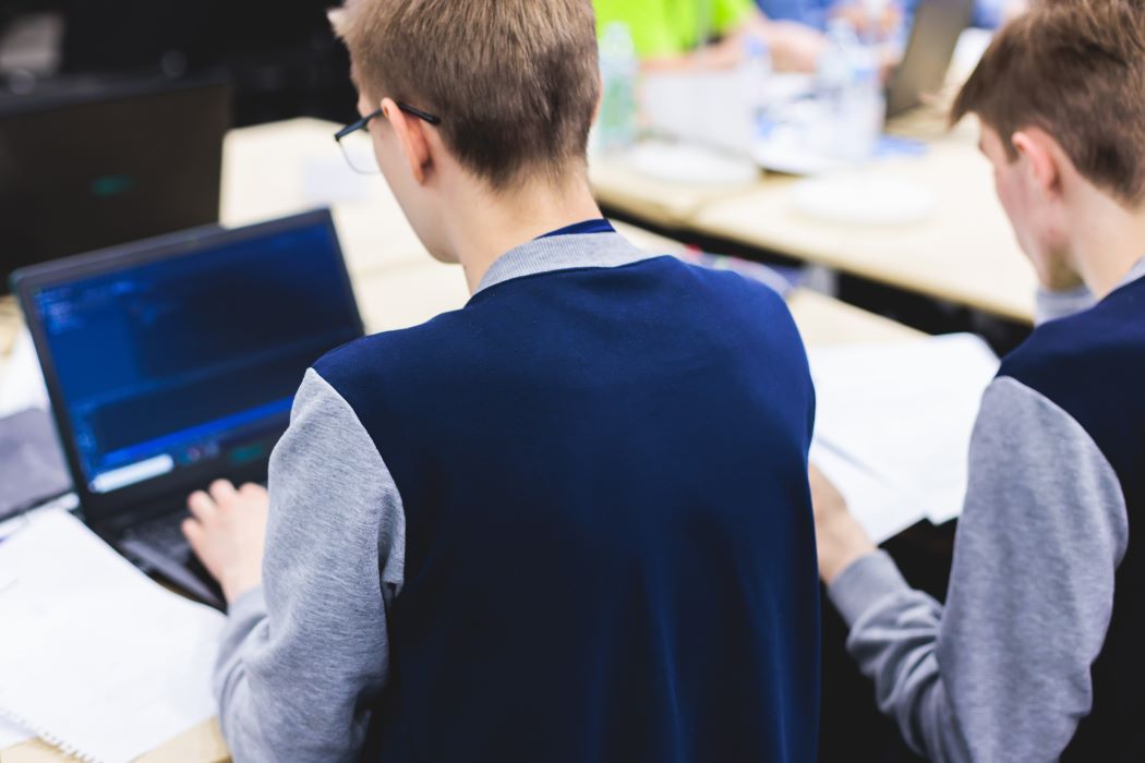 Un grupo de jóvenes vistos de espaldas trabajan en un proyecto tipo hackathon alrededor de un portátil