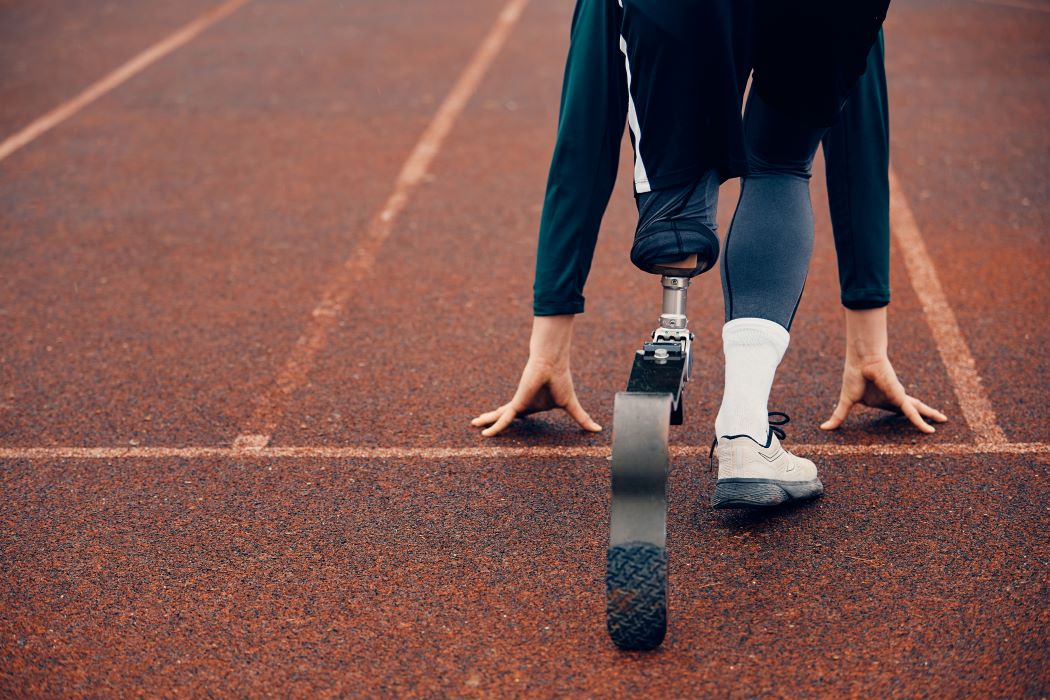 Persona con prótesis en una pierna colocada en posición de salida sobre una pista de atletismo.