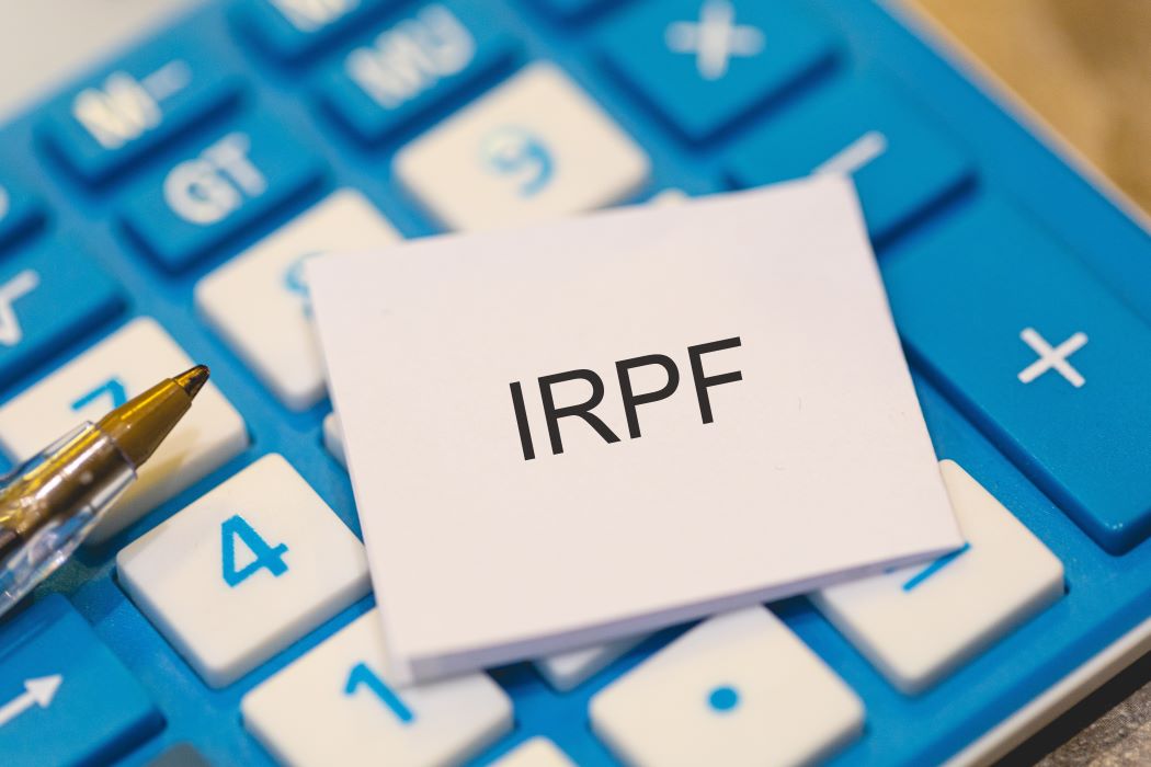 Tarjeta con la palabra “IRPF” sobre una calculadora azul, junto a un bolígrafo, que representa el cálculo de impuestos