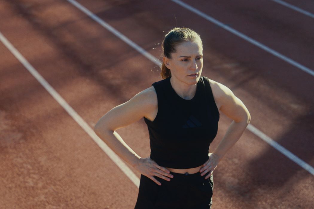 La atleta paralímpica Sara Andrés en una pista de atletismo con equipación deportiva negra, de pie en el carril y con las manos en la cintura tras una carrera