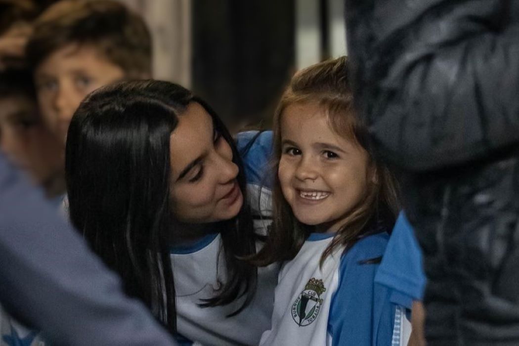 Una mujer adulta y una niña vestida con la equipación del Burgos FC hablan en el pasillo de vestuarios antes de salir al campo