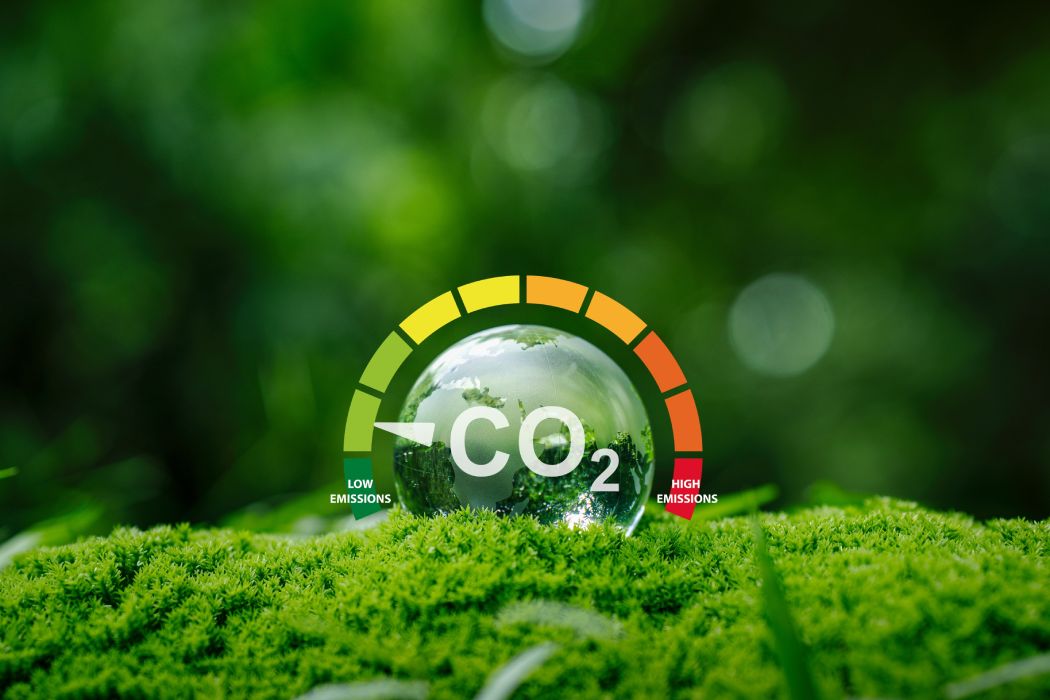 Primer plano de césped verde. Sobre él una esfera simula el globo terráqueo con las letras CO2. A su alrededor, un diagrama simboliza las emisiones bajas y hasta las altas de CO2