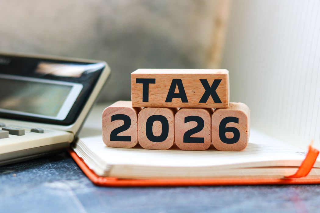 Blocs de fusta amb el text «TAX 2026» sobre una llibreta al costat d’una calculadora, simbolitzant la planificació i declaració d’impostos.