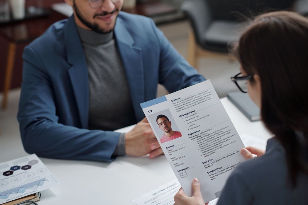 Entrevista laboral en oficina donde una persona revisa el CV impreso de otra, con gráficos y documentos sobre la mesa