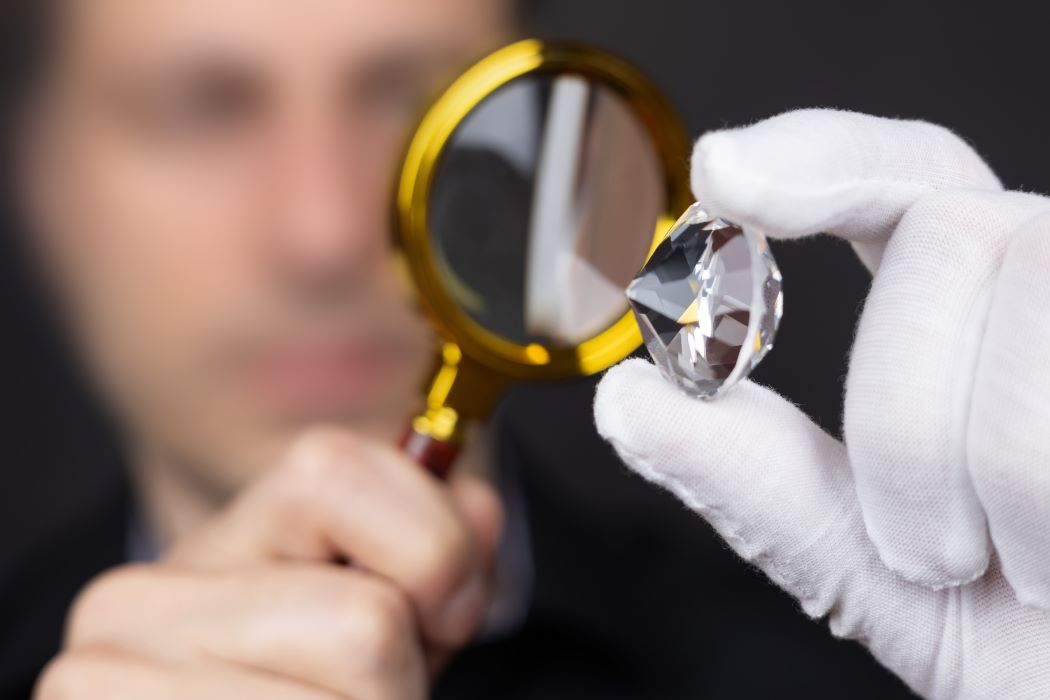 Una persona, con la cara difuminada, examina un diamante con una lupa y un guante blanco.