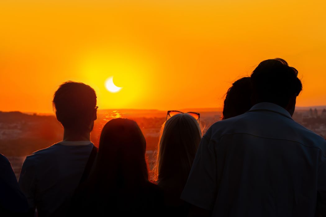 Vista de las siluetas de cinco personas de espaldas mirando al sol en un eclipse