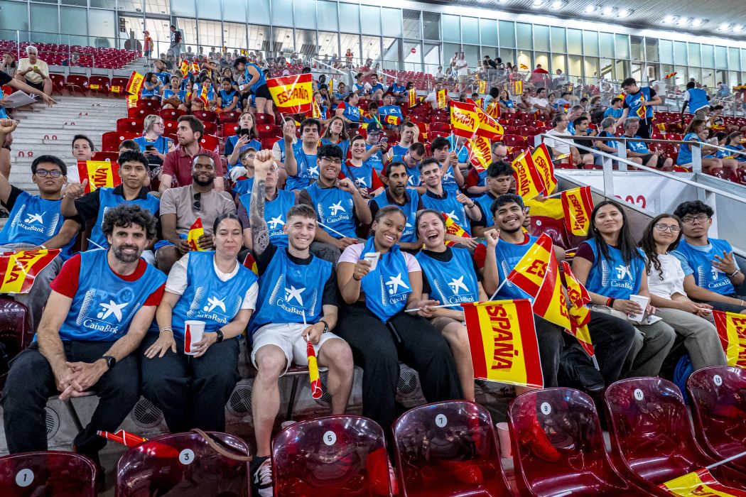 Grup de persones a les grades d’un estadi, amb samarretes blaves i banderes d’Espanya, participant en una activitat solidària en un ambient animat.
