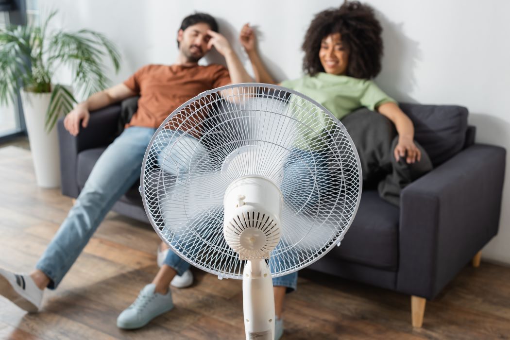 Una mujer joven y un hombre se refrescan delante de un ventilador mientras descansan en un sofá