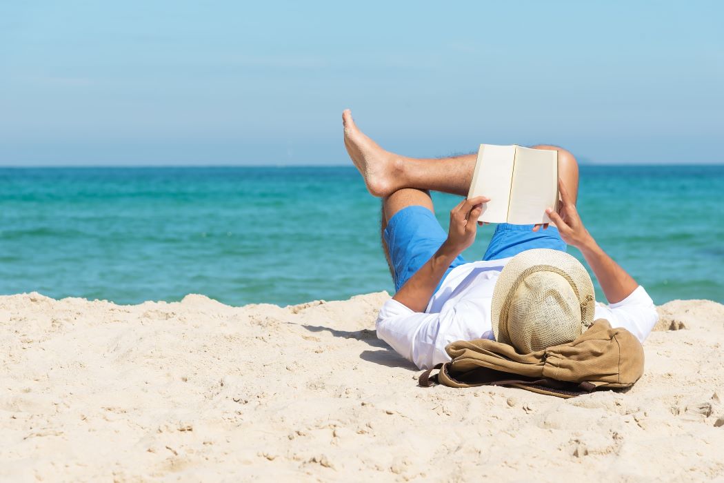 Una persona llegeix un llibre estirada en una platja