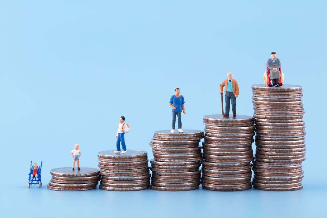 Piles de monedes en creixement amb figures de persones de diferents edats al damunt, representant l’evolució de la riquesa i l’estalvi al llarg de la vida